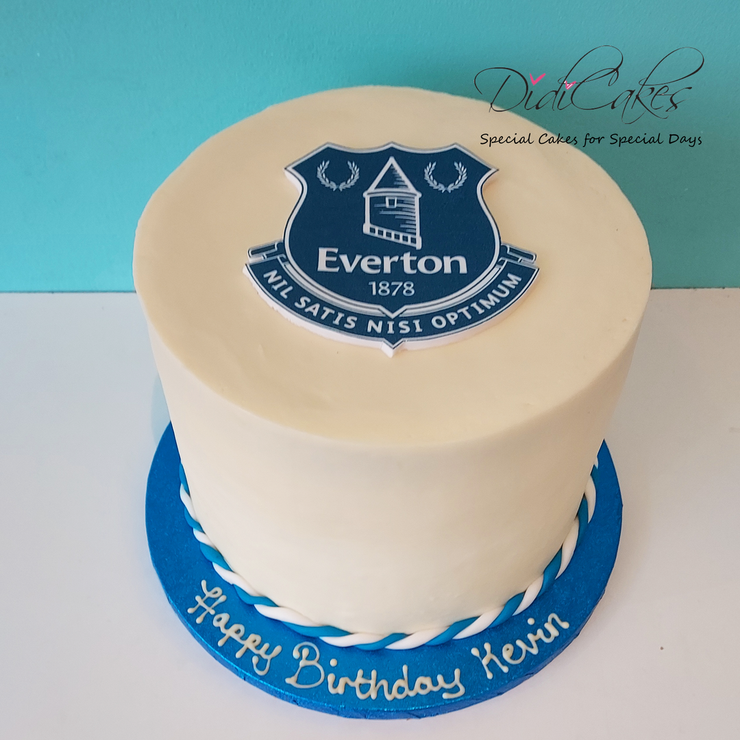 A round cake with blue and white icing, decorated with a crest that represents a football club. Premier league team colours